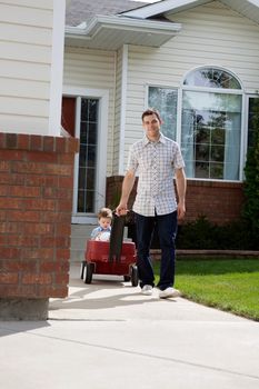 Father pulling son sitting with a ball in pram down a walkway