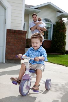 Toddler boy learning to ride tricycle with father in background