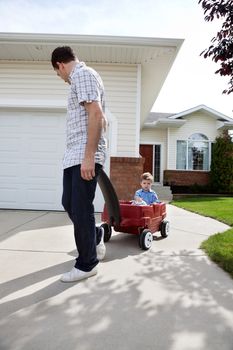 Father pulling son in wagon in front of house
