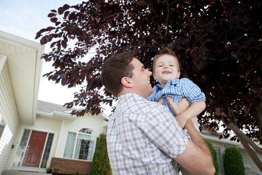 Father Lifting His Little Adorable Boy In Front Of House.