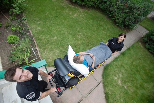 Above view of an emergency medical team pushing stretcher with senior woman in a residential area.