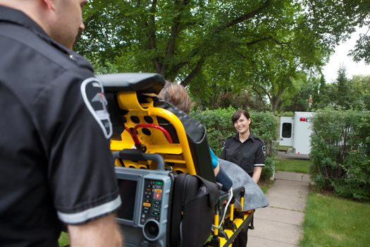 Two ambulance workers pushing elderly patient to vehicle