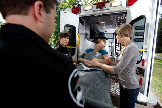 Paramedic team placing senior woman in ambulance, caregiver at side