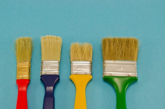 different colors and size paint brush construction tools on blue background.