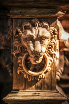 Face of a carved wooden lion, which is illuminated by the sun.