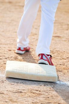 Lower body shot of baseball boy standing on a base.