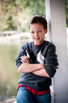 A cute young boy posing next to a pole in front of a pond.