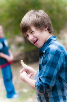 A young boy pointing backwards at someone and winking.