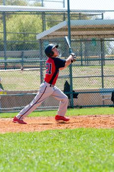 Teen boy baseball player watching ball after his hit.