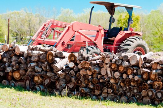 Stack of firewood with tractor in background.