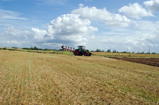 tractor prepared for plow stand near agricultural harvested field.