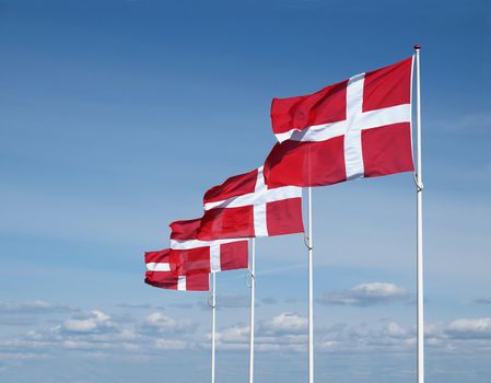 four flapping danish flags on clear blue sky