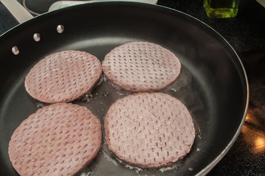 Four hamburgers in a hot frying pan.