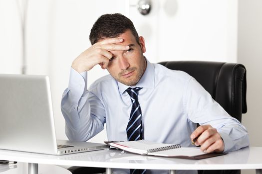 pensive man in office with computer and pen