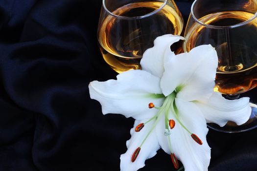 Glasses with wine and lily flower on black silk