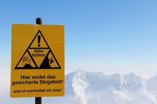 Danger sign in Mountains with panoramic view of winter alps under blue sky
