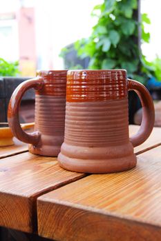 Two clay mugs of beer on wooden table in restaurant