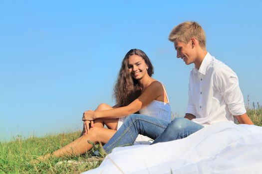 Young couple sitting on summer field discussing something and smiling