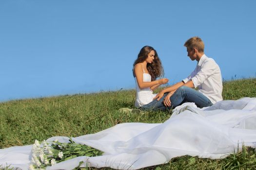 Young couple sitting on summer field discussing something and smiling