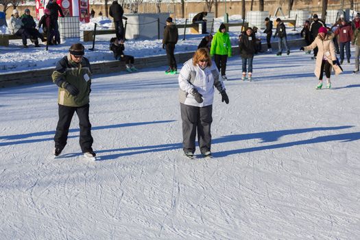 An overweight woman and and elder are trying to learn how to ice skate in a really cold winter day in the Skating Rink in Old Port of Montreal, Quebec ,Canada