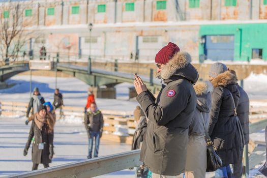 A woman taking a picture with her phone in a cold winter day in the Skating Rink in Old Port of Montreal. Quebec, Canada