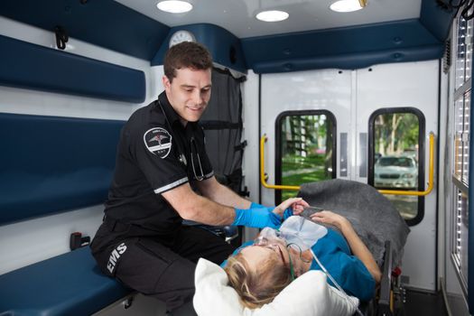 Male EMT professional taking pulse of a senior woman inside ambulance