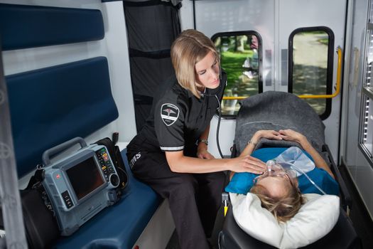 Female EMT worker tending to ill senior patient, listening to heart rate with stethoscope