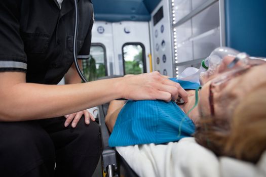 Detail of EMT worker listening to heart of senior woman patient in ambulance