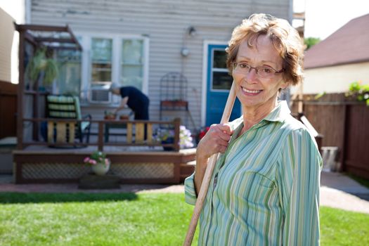 Portrait of elderly woman holding gardening tool with friend in the background