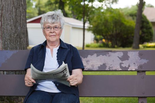 Portrait of senior woman holding newspaper, sitting on park bench