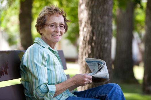 Portrait of smiling elderly woman reading newspaper in park