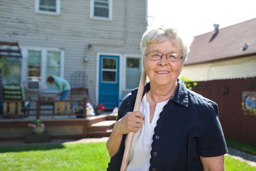 Portrait of senior woman holding gardening tool with friend in the background