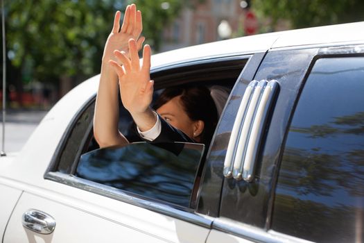 Happy newlywed couple waving out of limousine window