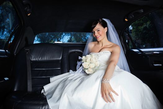 Beautiful bride sitting in car holding flower bouquet