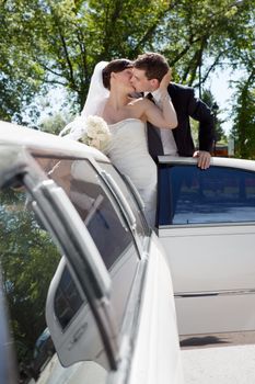 Newlywed Couple Standing Beside Limousine Car Kissing Each Other Holding Bouquet In Hand.