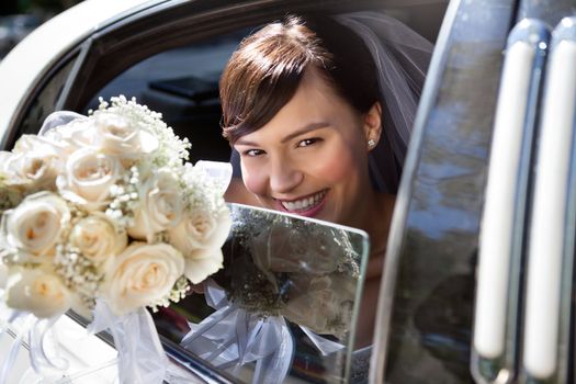 Happy bride sitting in limousine holding out flower bouquet