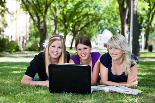 Portrait of three students working on laptop on campus ground