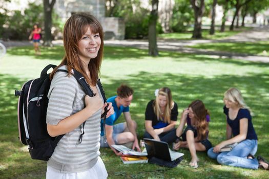 Portrait of young college girl at college campus with classmates studying in background