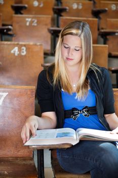 Lifestyle shot of young college girl reading a text book in a lecture hall