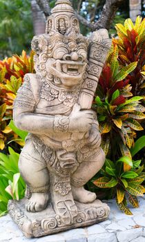 Thai stone god in the bushes of tropical plants. Short depth of field.