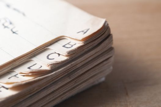 Close up of an old, index tabbed address book with yellowing and furled pages, placed on a wooden table with light coming from left of frame and some shadow to the right.