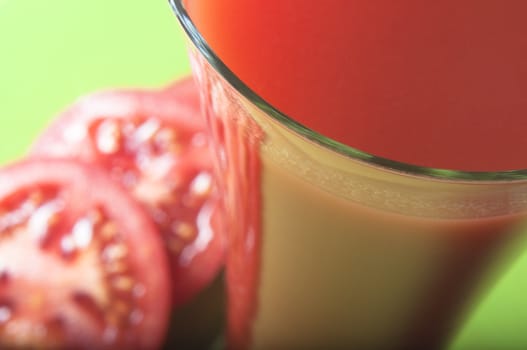 Macro (close up) shot of a tall glass of tomato juice, taken from above, with tomato slices in soft focus beside the glass.  Fresh green background.