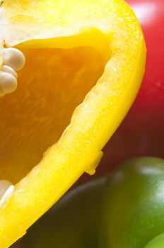 Close up (macro) shot of three bell peppers with yellow variety cut open in the foreground, exposing seeds.