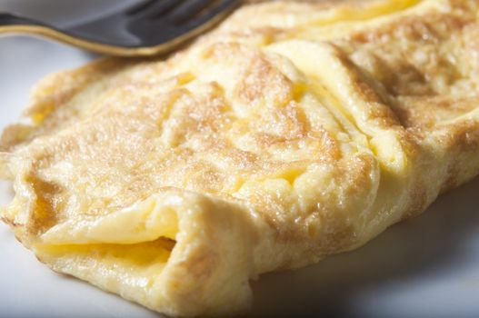 Close up (macro) of a cooked omelette, served on a white china plate with stainless fork in background.  Shallow depth of field.