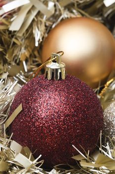 Close up of red sparkly Christmas bauble, nestling among gold tinsel garlands, with matte gold bauble in background.  Differential focus.