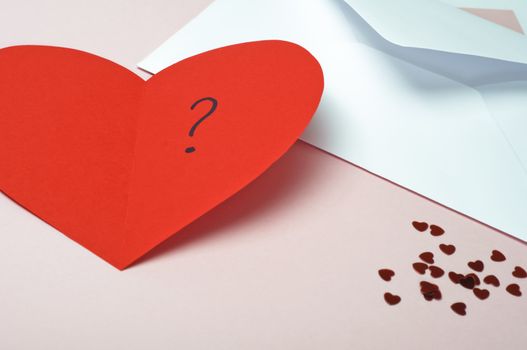 A red heart-shaped Valentines card, opened to reveal a question mark.  Small metallic hearts scattered at bottom right, with white open envelope at top right.  Pink background with copy space.