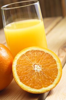 Close up of a glass of orange juice with cut and whole oranges on wooden table.