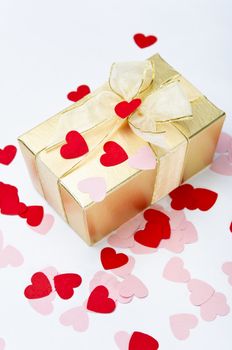 A gold gift box, bow tied with organza ribbon, sprinkled with pink and red paper heart-shaped confetti.