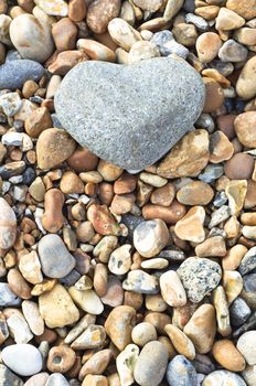 A grey heart shaped stone in upper frame, resting on a variety of smaller stones.  Portrait (vertical) orientation.