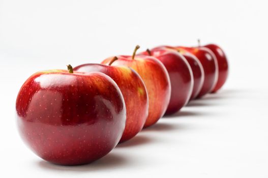 Close up of a row of seven shiny red apples leading away from the viewer at an oblique apple.